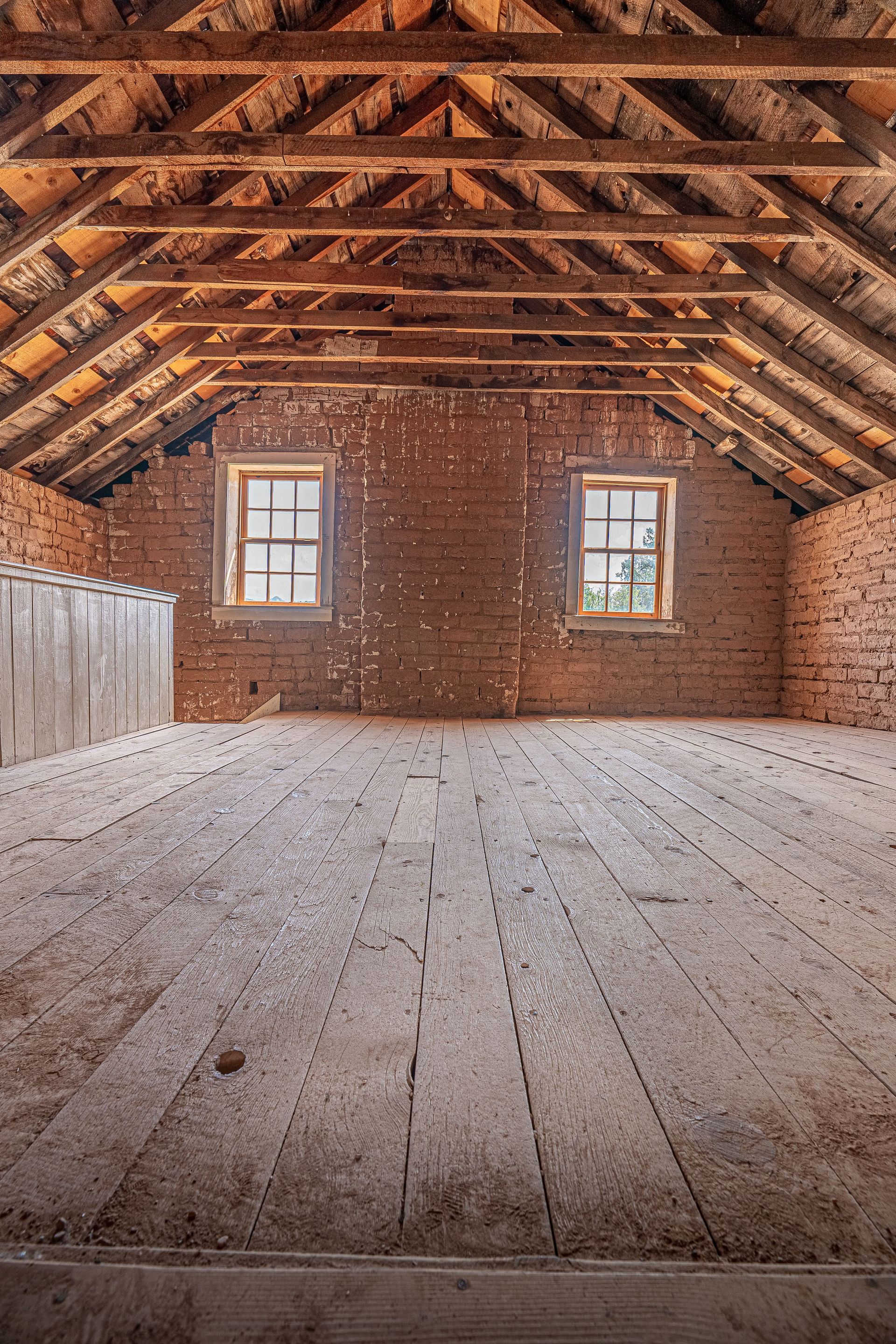 Spacious attic interior featuring exposed wooden beams and brick walls, perfect for renovation or design inspiration.
